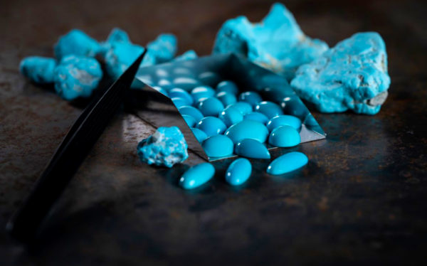 Polished treated turquoise. In the background, raw turquoise from mining.